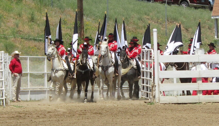 The horses kick up dust as they and their riders enter the rodeo grounds.